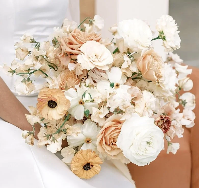 A person holding a large bouquet of light-colored and white flowers, including roses, poppies, and other blossoms.