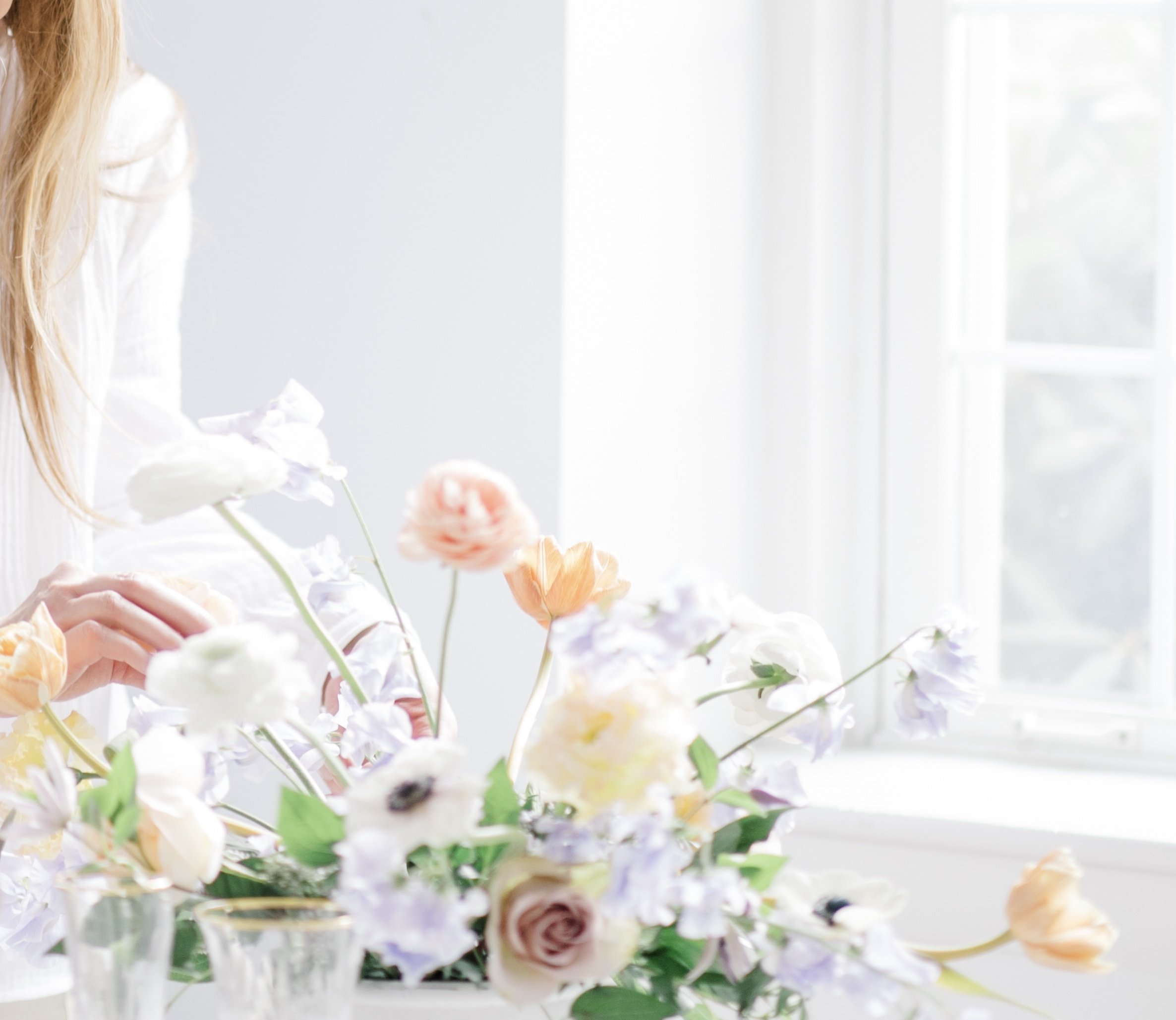 A person arranging a colorful bouquet of flowers near a large window.
