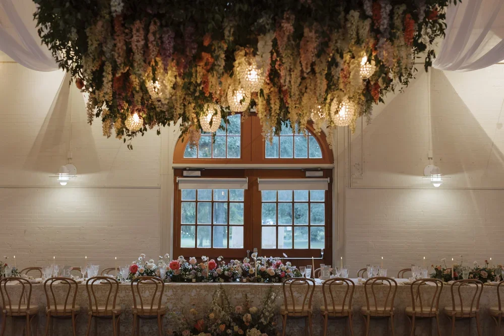 A decorated banquet hall with a long table, floral arrangements, and a large floral chandelier hanging from the ceiling.