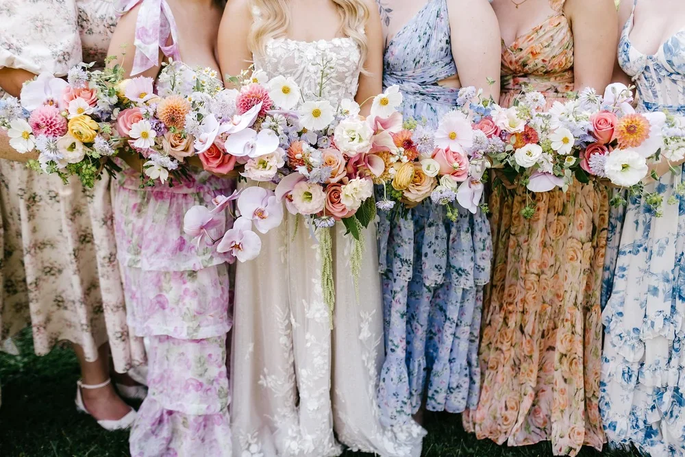 Group of women in floral dresses holding large colorful bouquets of flowers at a wedding or celebration.