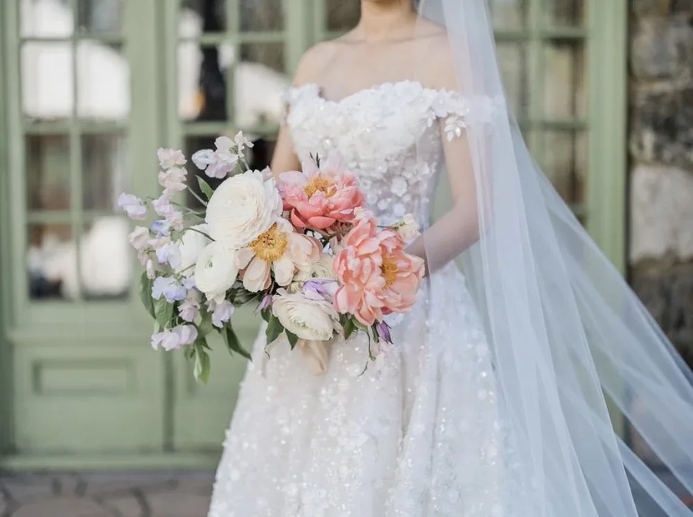 Bride in white wedding dress holding a large bouquet of pink, white, and purple flowers.