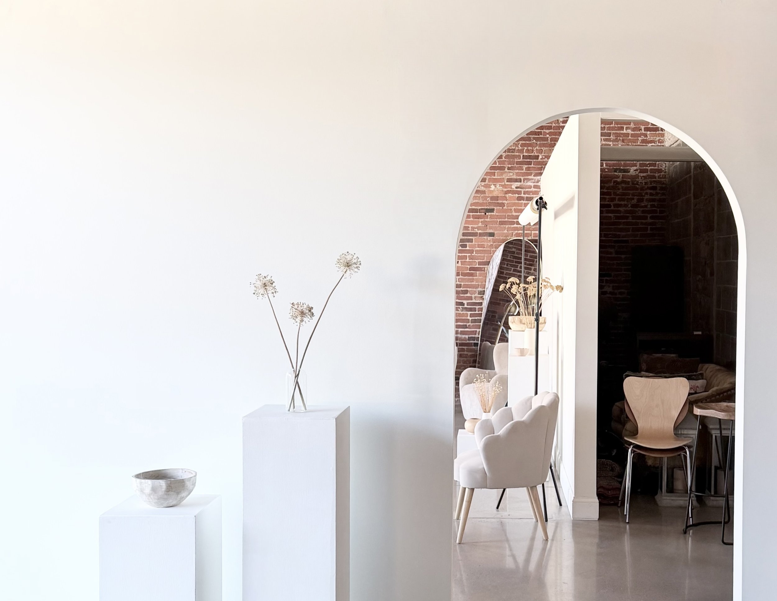 Modern interior with white walls, minimalist decor, and arched doorways leading to a cozy space with brick walls and eclectic furniture.