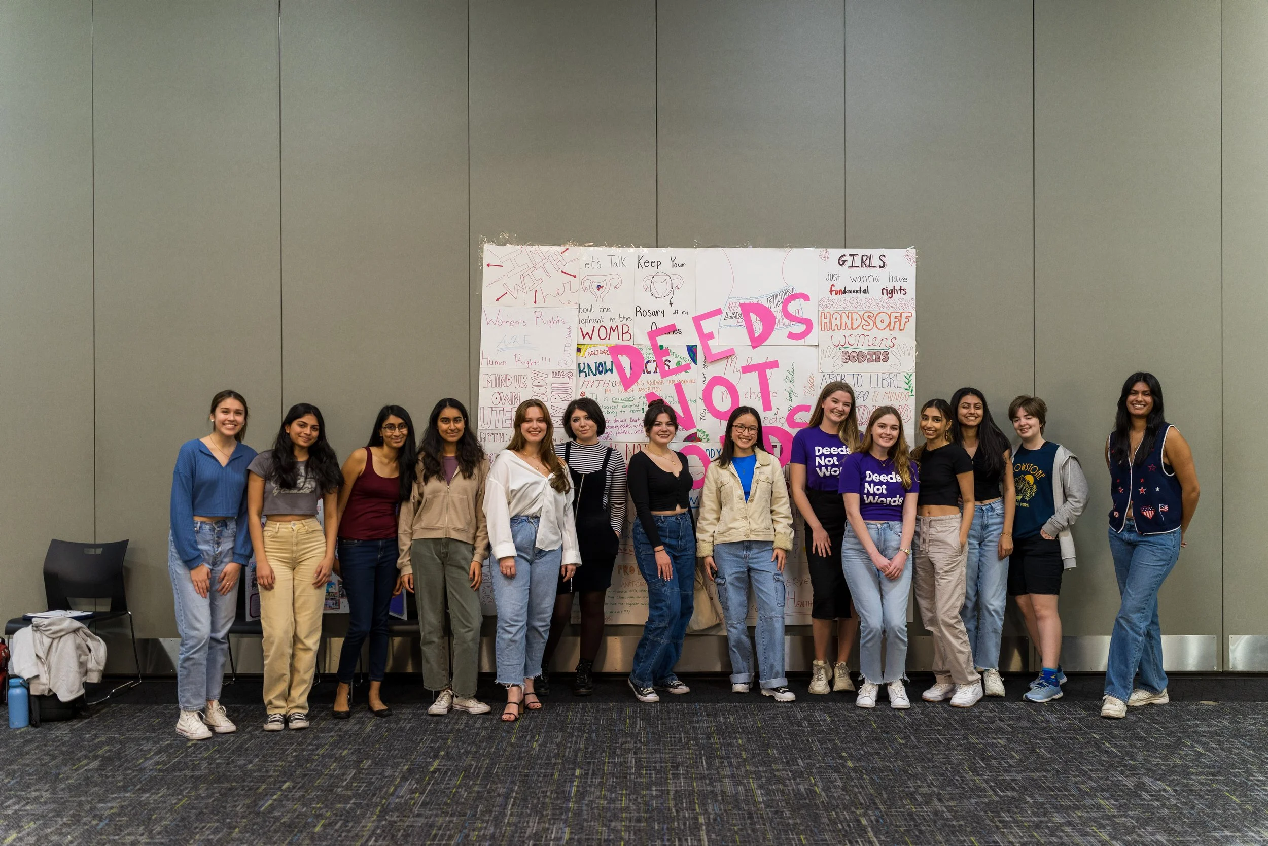 Deeds Not Words students gather in front of a sign that reads "Deeds Not Words"