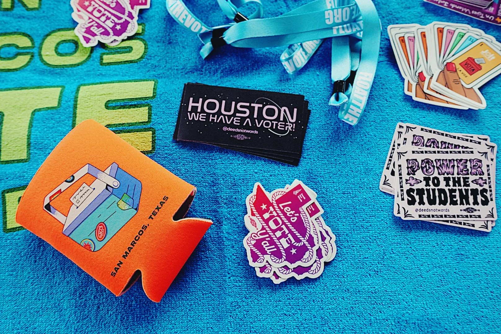 Deeds Not Words and other partner organization merch and stickers on a blue towel that reads "Float the Vote".