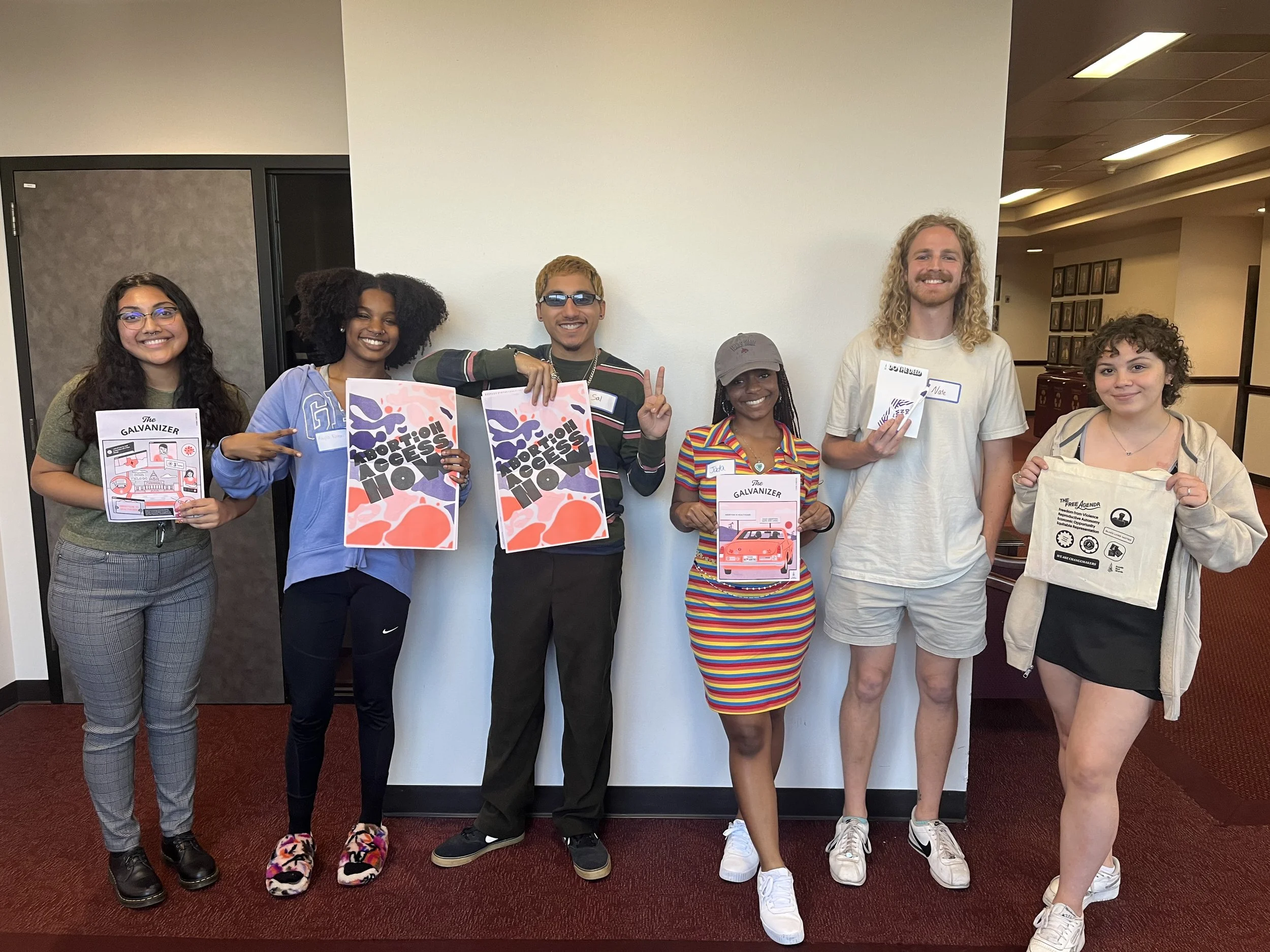 Students gather to take a picture with Deeds Not Words zines, posters, and totes