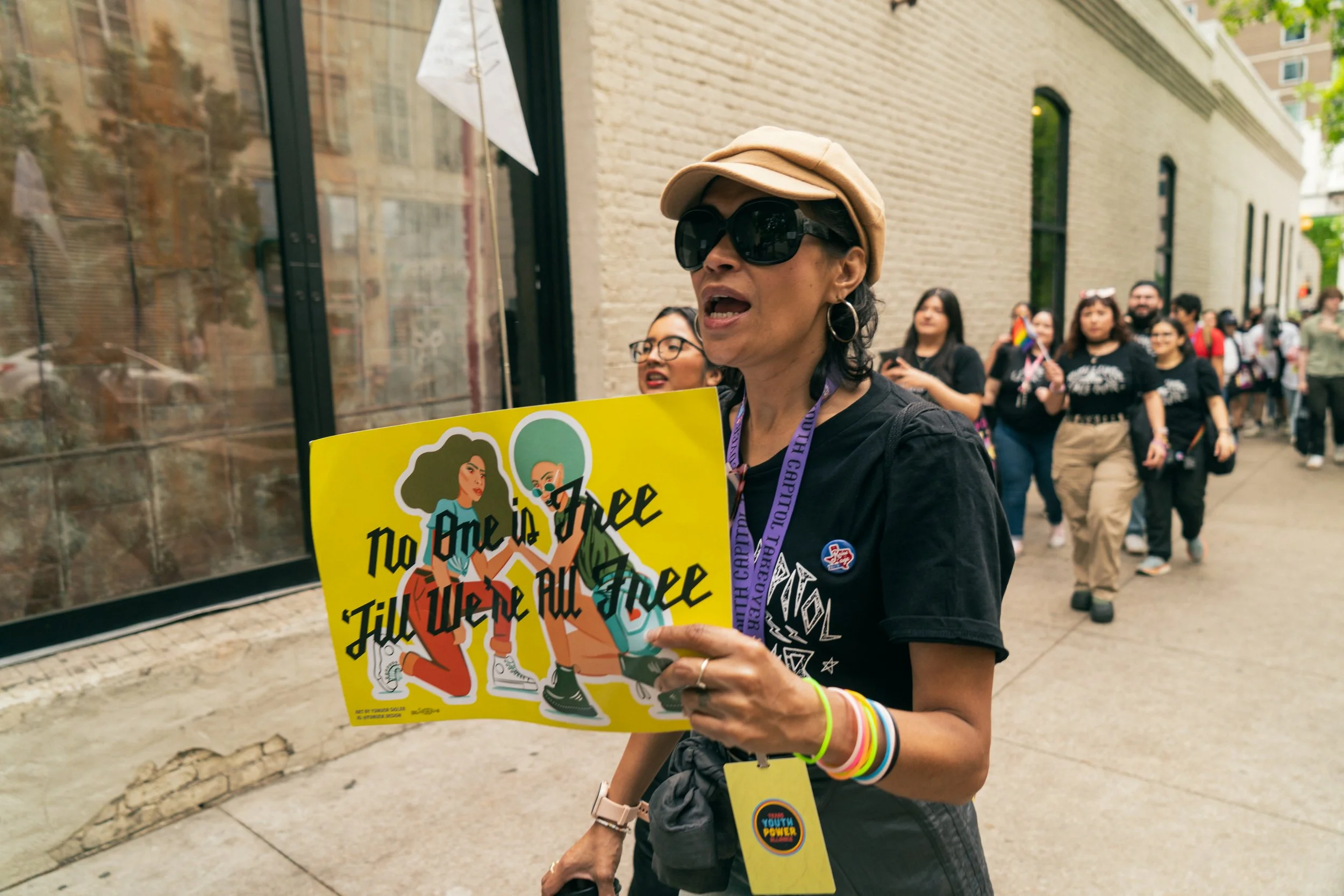 A person holds a sign that reads "No One is Free 'till We're All Free"