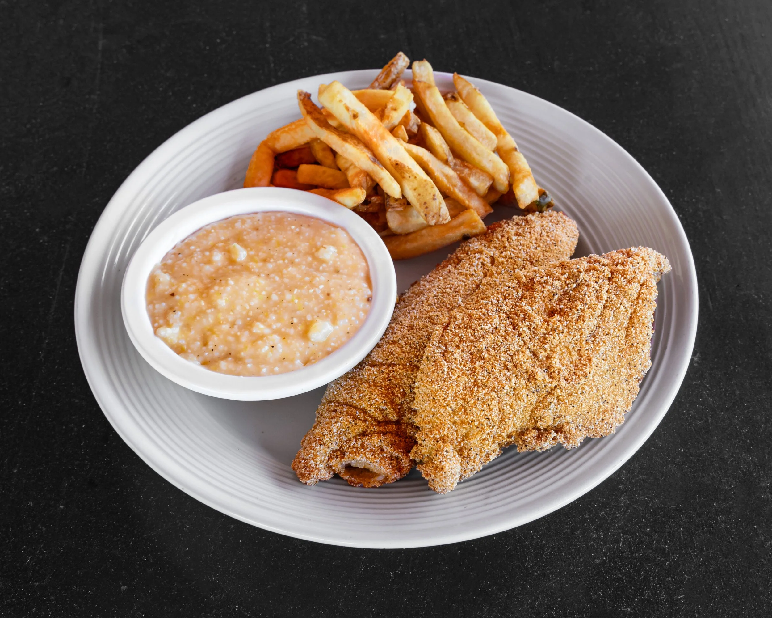 Fried fish fillets with fries, a bowl of baked beans, and a hot dog bun on a white plate