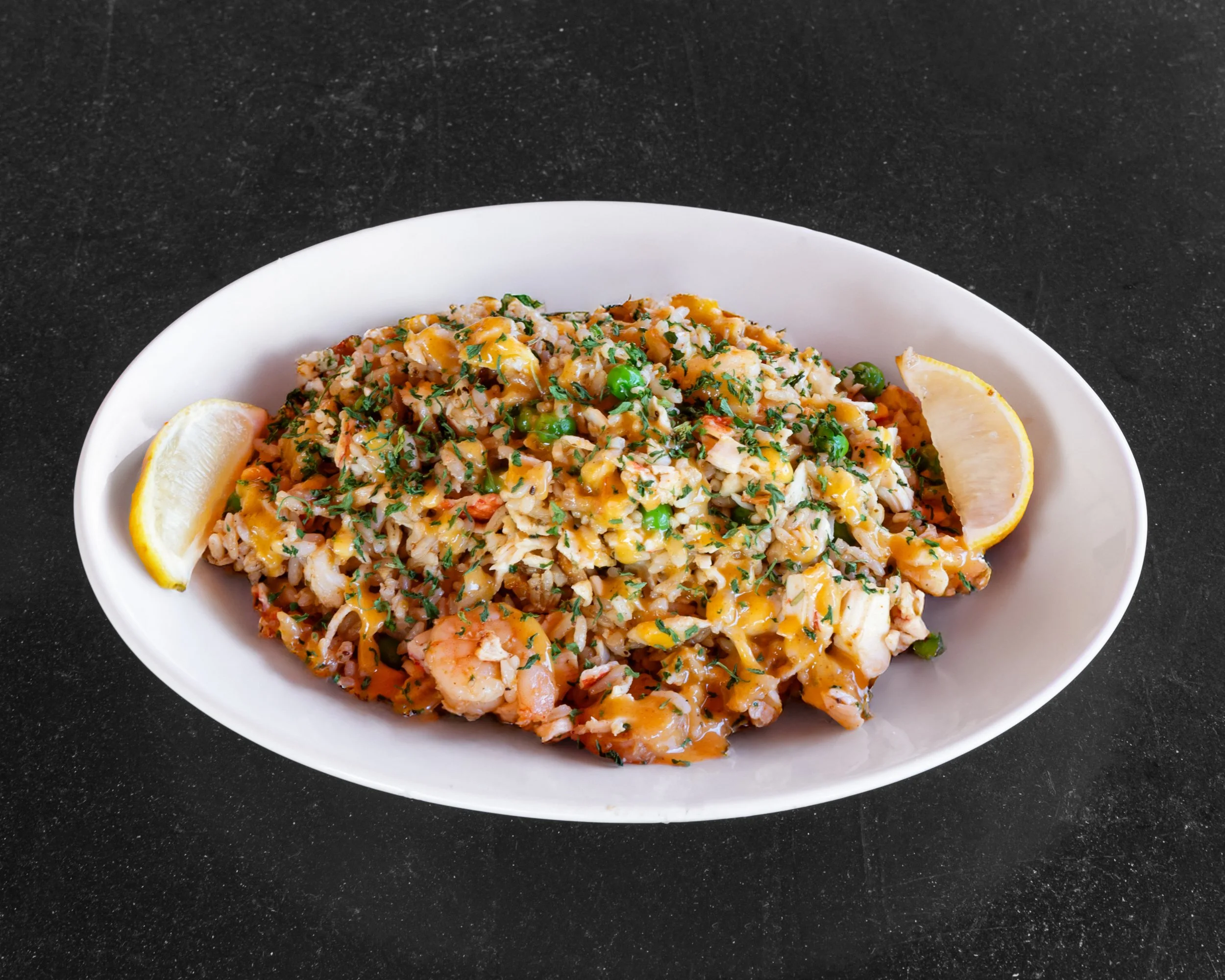 Seafood fried rice served in a white oval dish with lemon wedges on the side, garnished with chopped herbs.