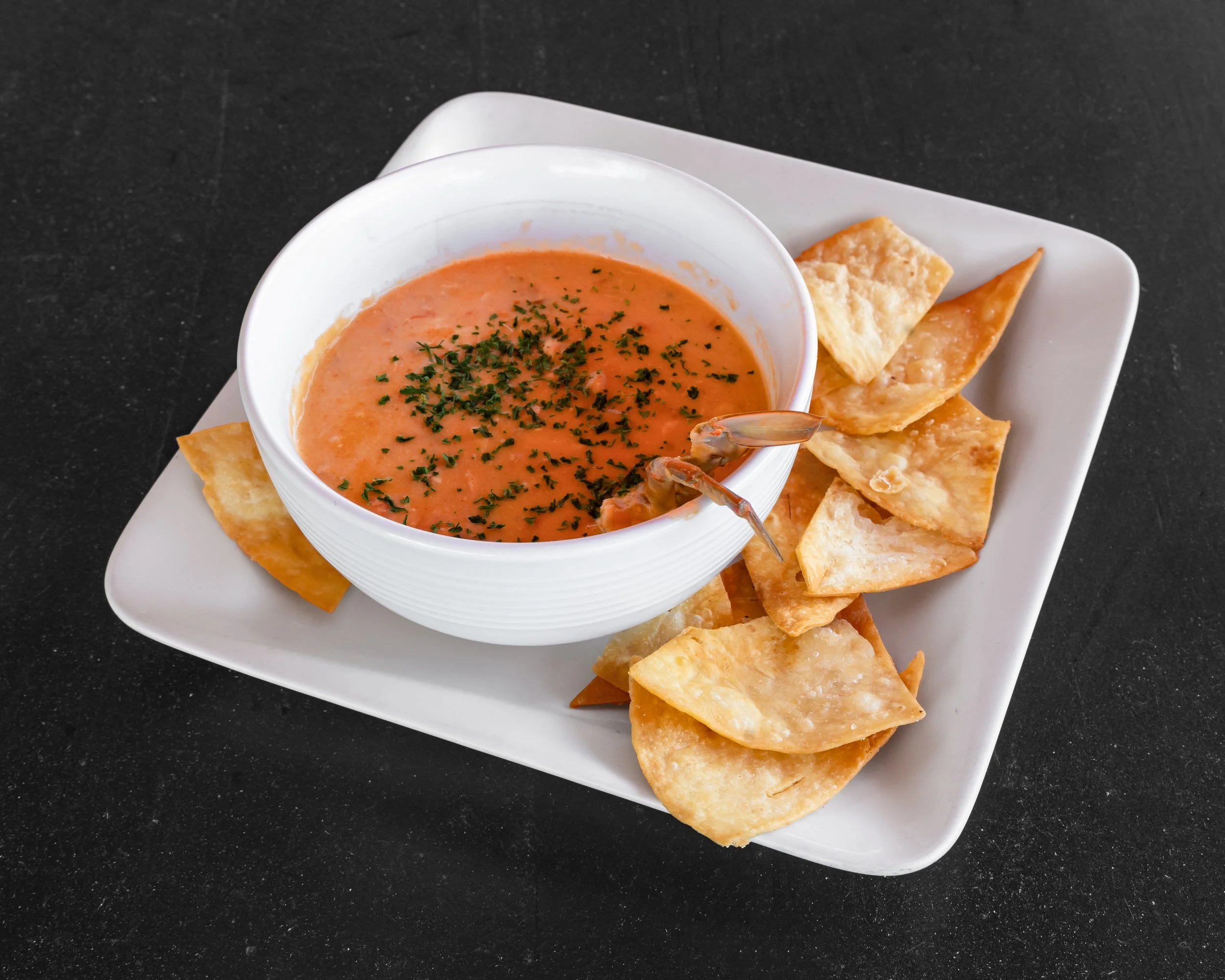 Bowl of shrimp cocktail garnished with chopped herbs, served with tortilla chips on a white square plate