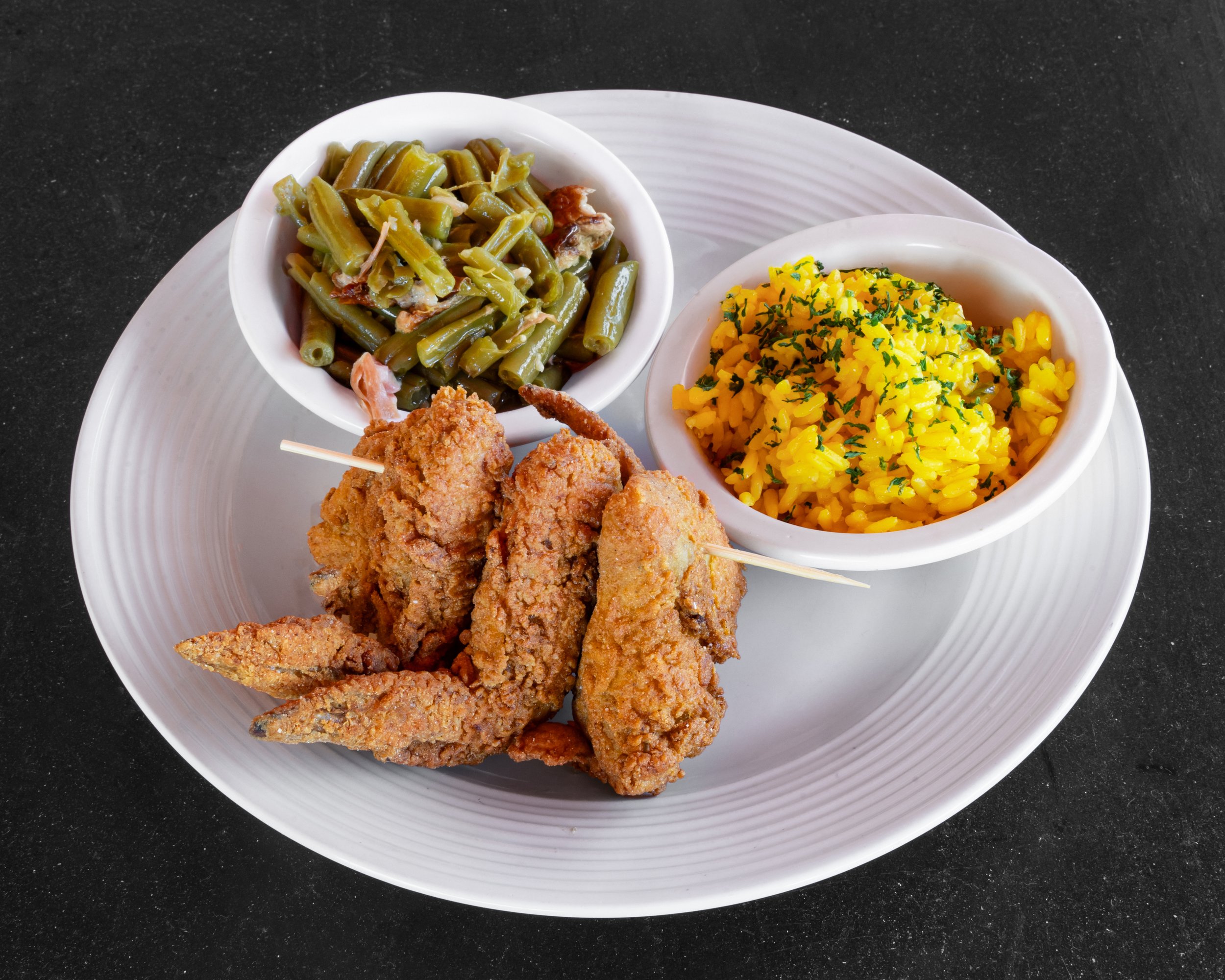 Fried chicken wings, yellow rice with herbs, and green beans on a white plate.
