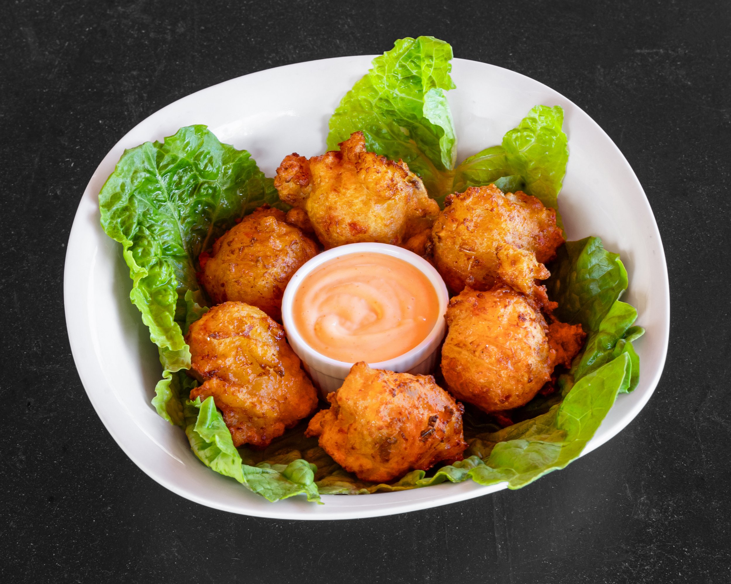 Bowl of fried chicken pieces on a bed of lettuce with dipping sauce.
