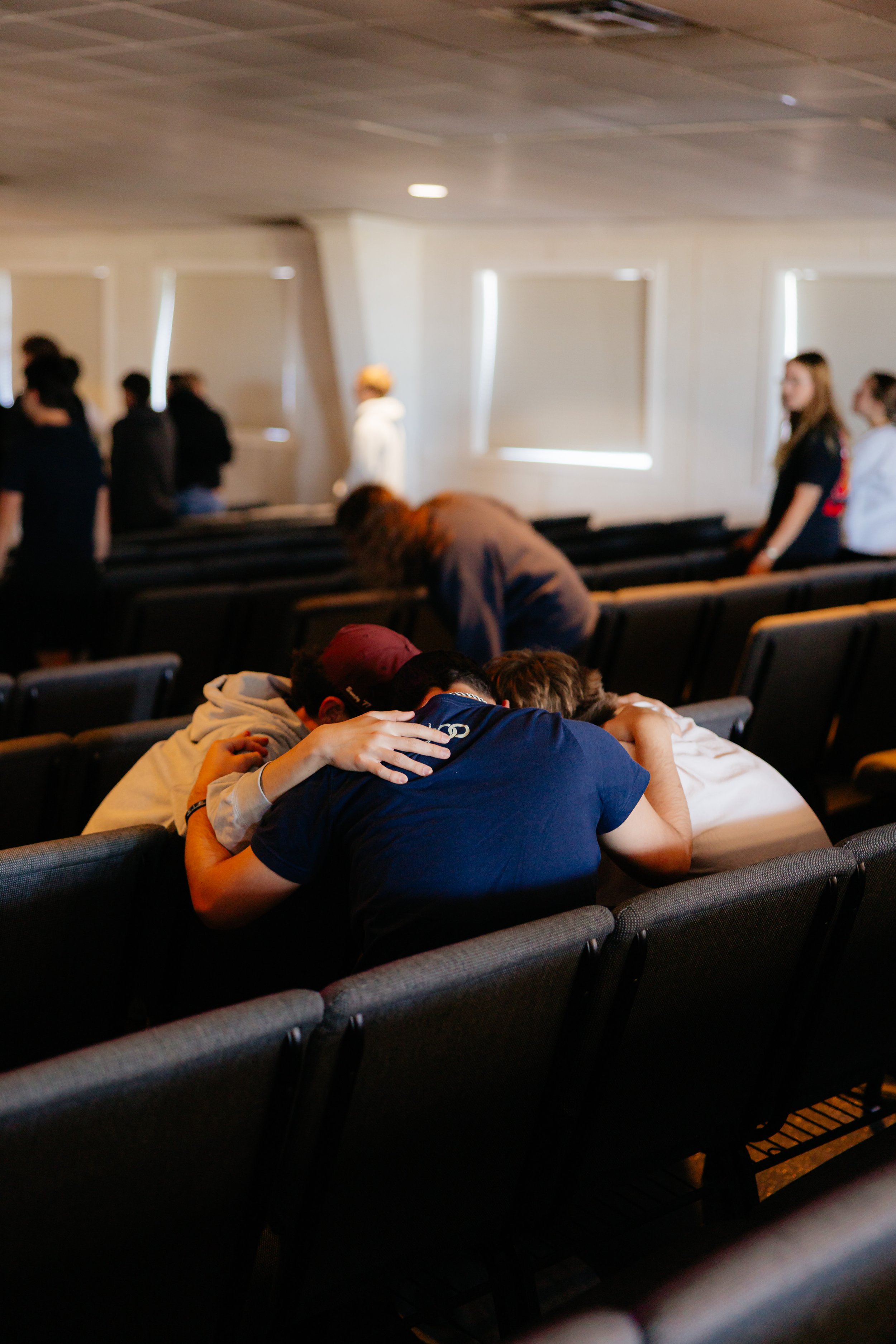 A group of people seated in a row, engaged in hugging and comforting each other in prayer.