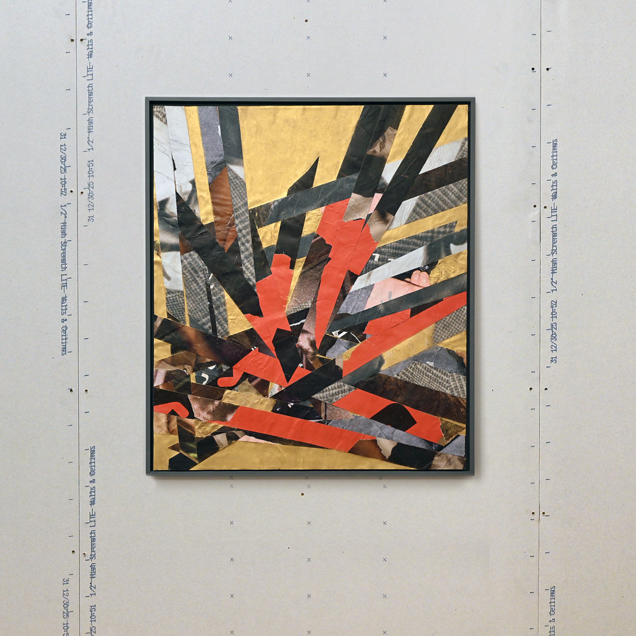 Abstract collage artwork with black, red, and gold, mounted in a dark grey frame,