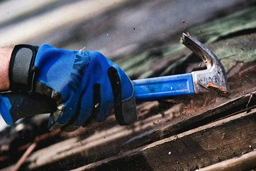 Close-up of a person wearing a blue glove using a hammer to break wood.
