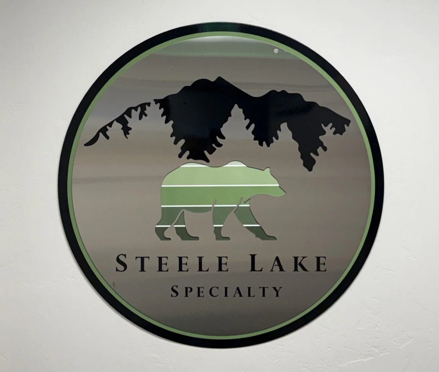 Logo of Steele Lake Specialty featuring a bear silhouette with a mountain range inside, set against a reflective surface.