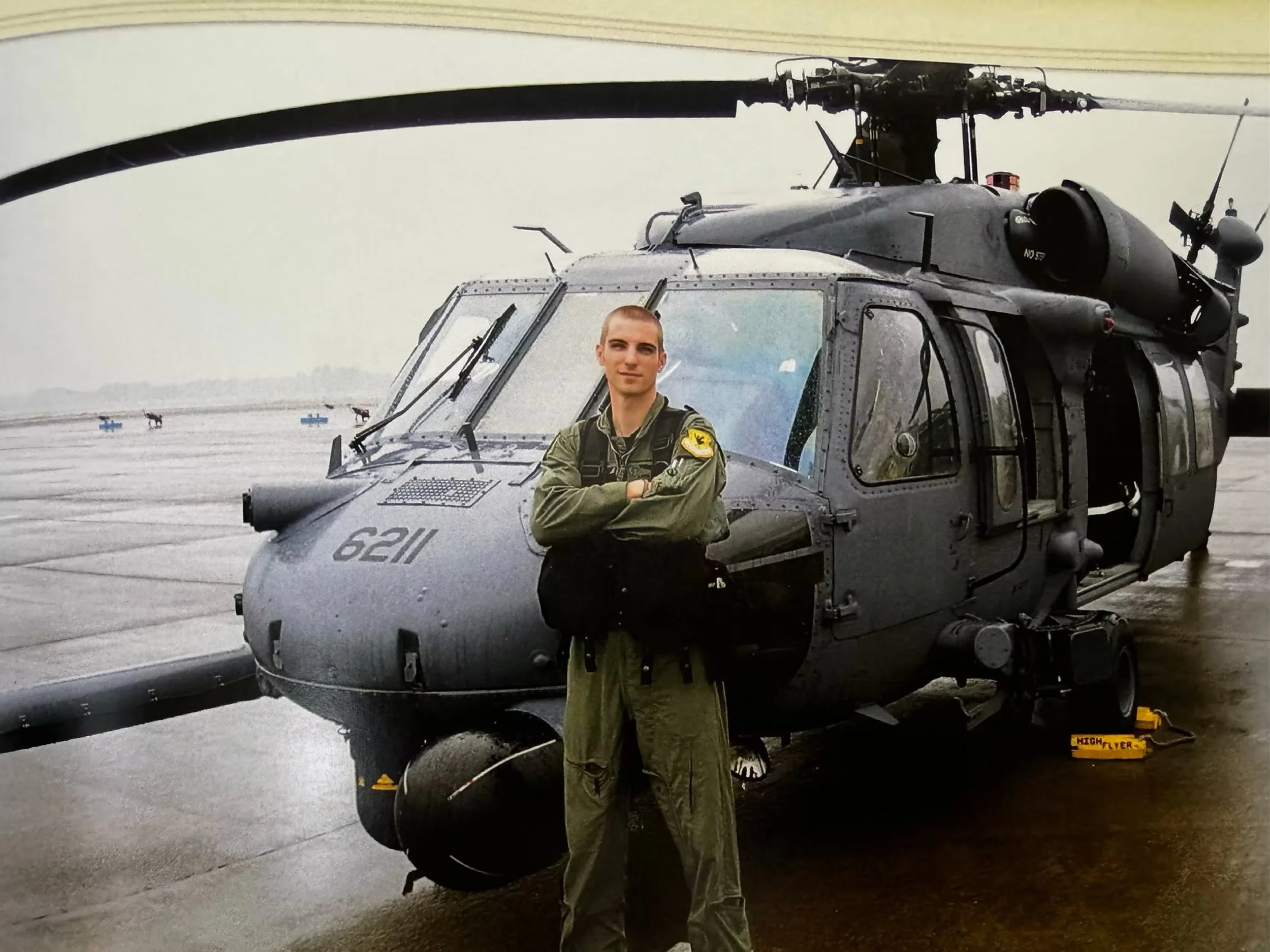 A person in military attire standing in front of a military helicopter on an airfield.