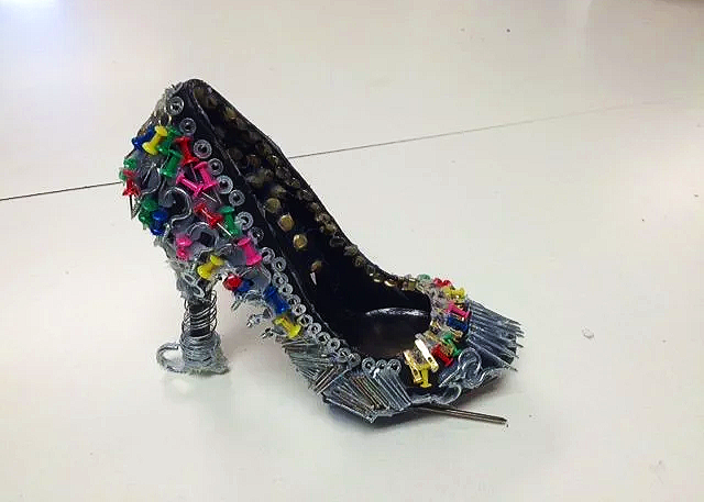A high-heeled shoe sculpture made from various nails, screws, and small colorful plastic parts, resembling a decorated shoe.
