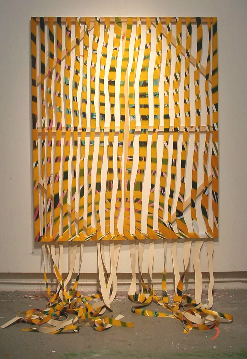 An abstract art piece with vertical yellow, white, and multicolored strips hanging from a square canvas, creating a layered, textured appearance. The strips extend to the floor, curling and scattering at the bottom.