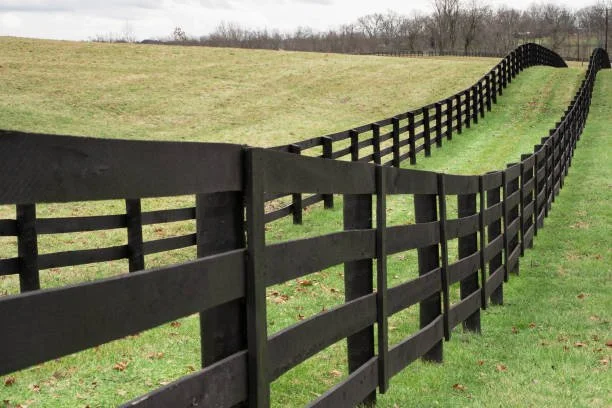 Black wooden fence running along a grassy hill, creating a wavy pattern