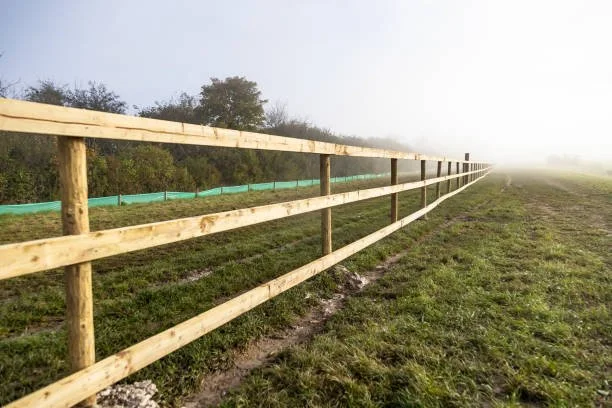 Post and rail fence along a grassy field with fog in the distance.