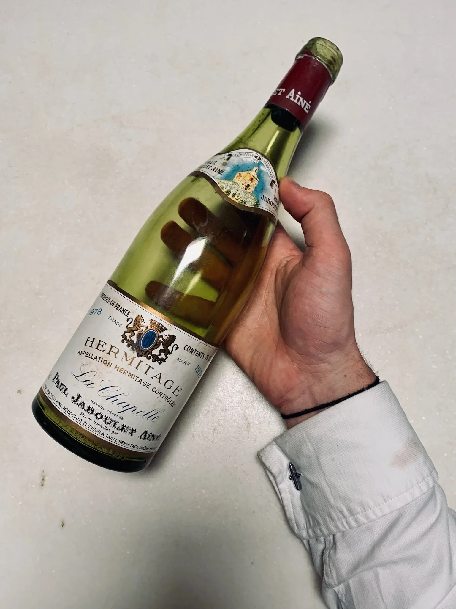 A hand holding a bottle of Hermitage La Chapelle wine with a white background.