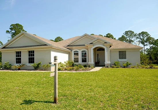 Front view of a single-story house with a green lawn, small shrubs, and a mailbox in the foreground.