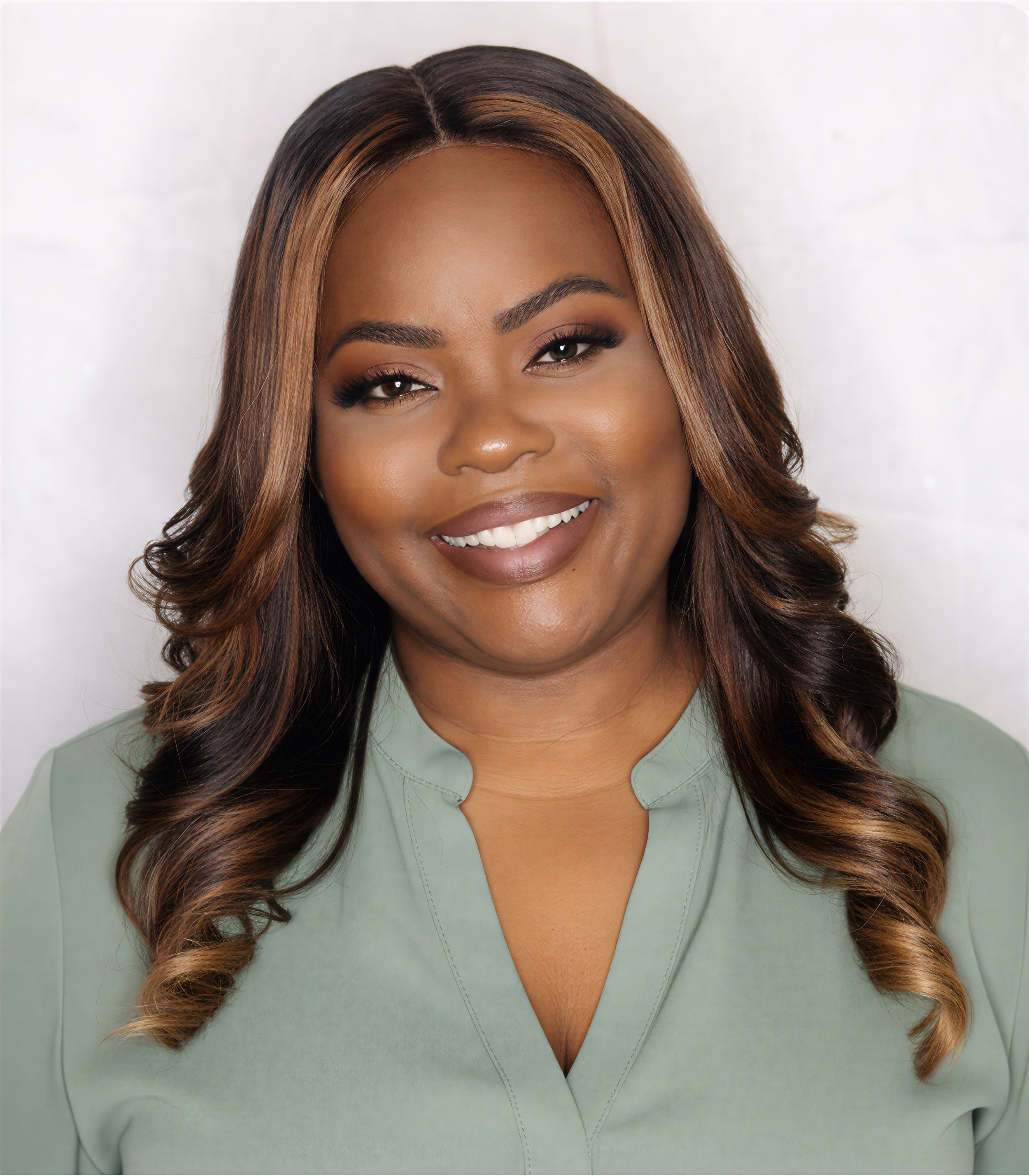A smiling woman with brown and blonde hair styled in loose curls, wearing a green blouse, against a white background.