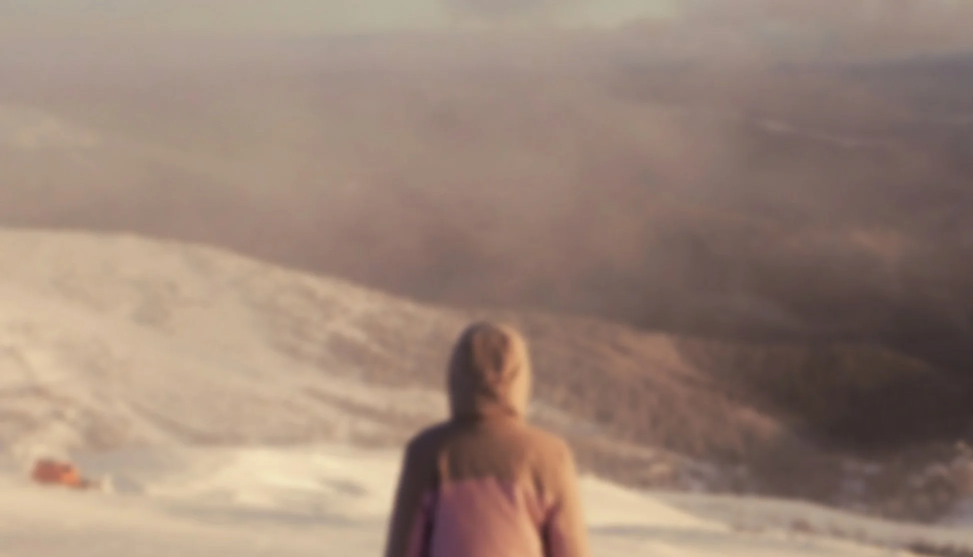 Person standing in snow-covered landscape, facing away, under cloudy sky.