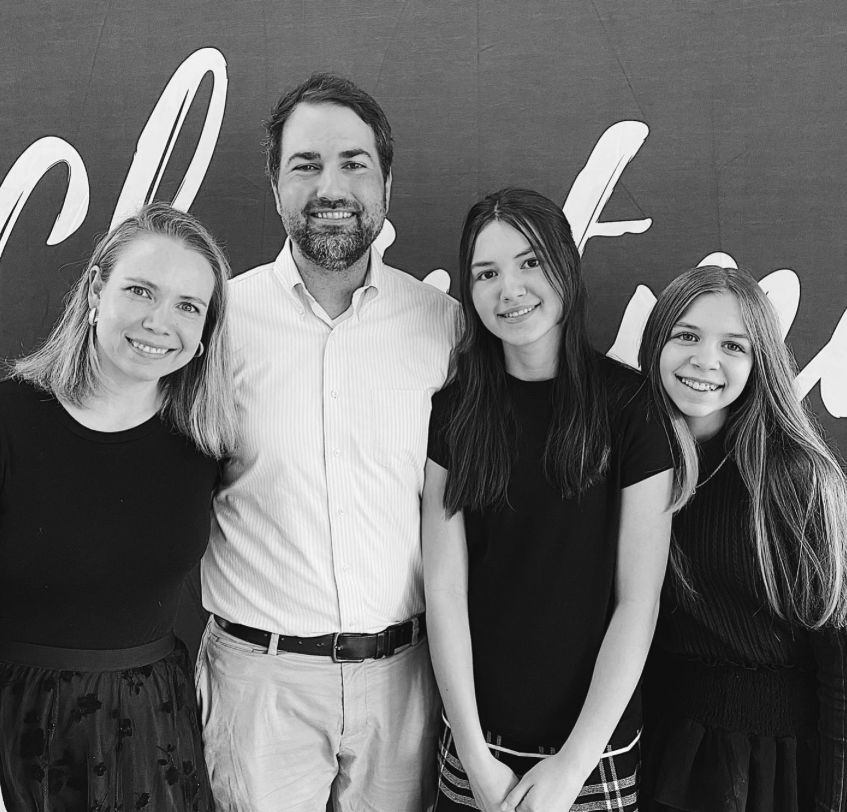 Four people, two women, one man, and one girl, smiling and posing in front of a wall with large decorative writing.