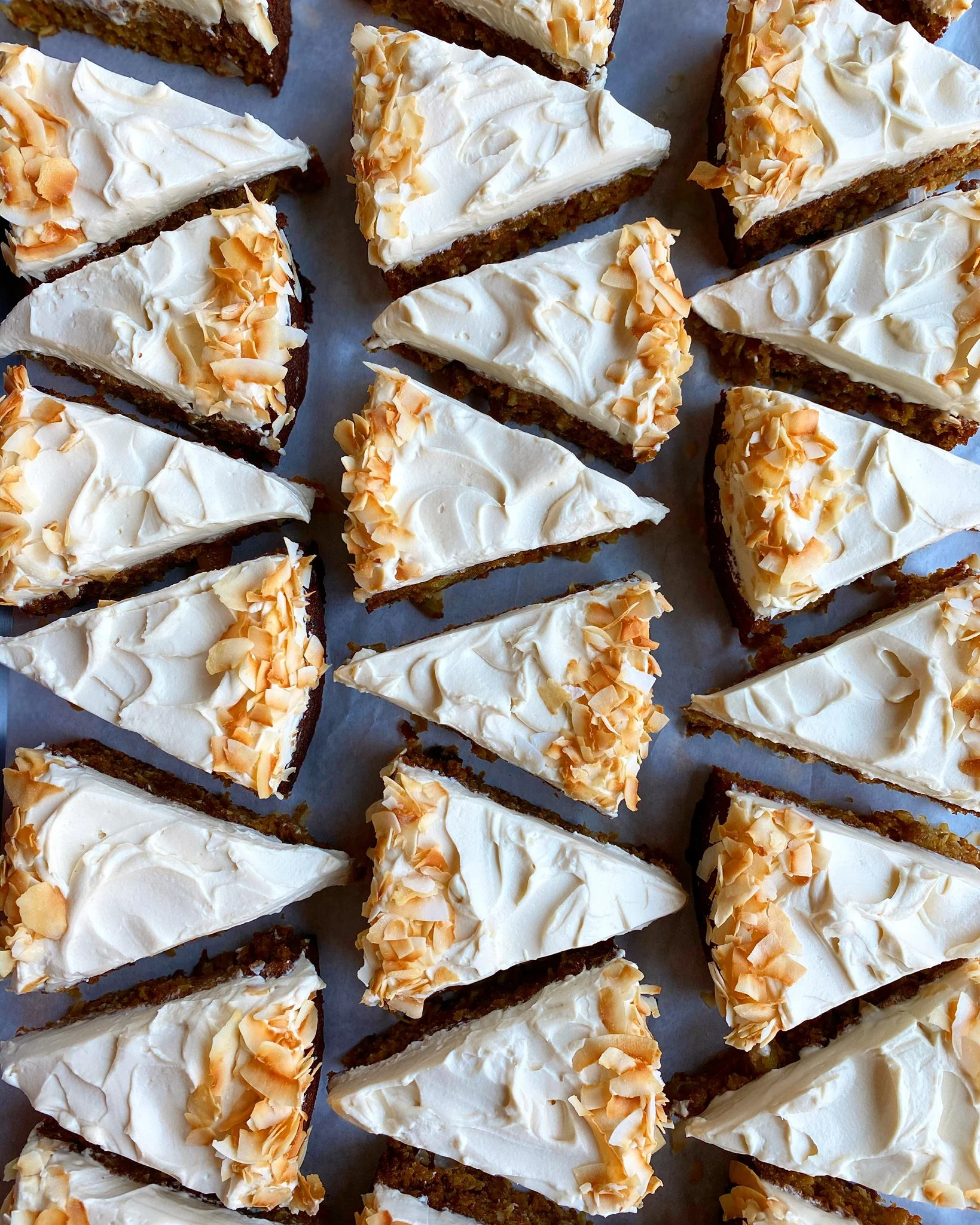 Slices of cake with white frosting and almond flakes on top, arranged on a sheet.