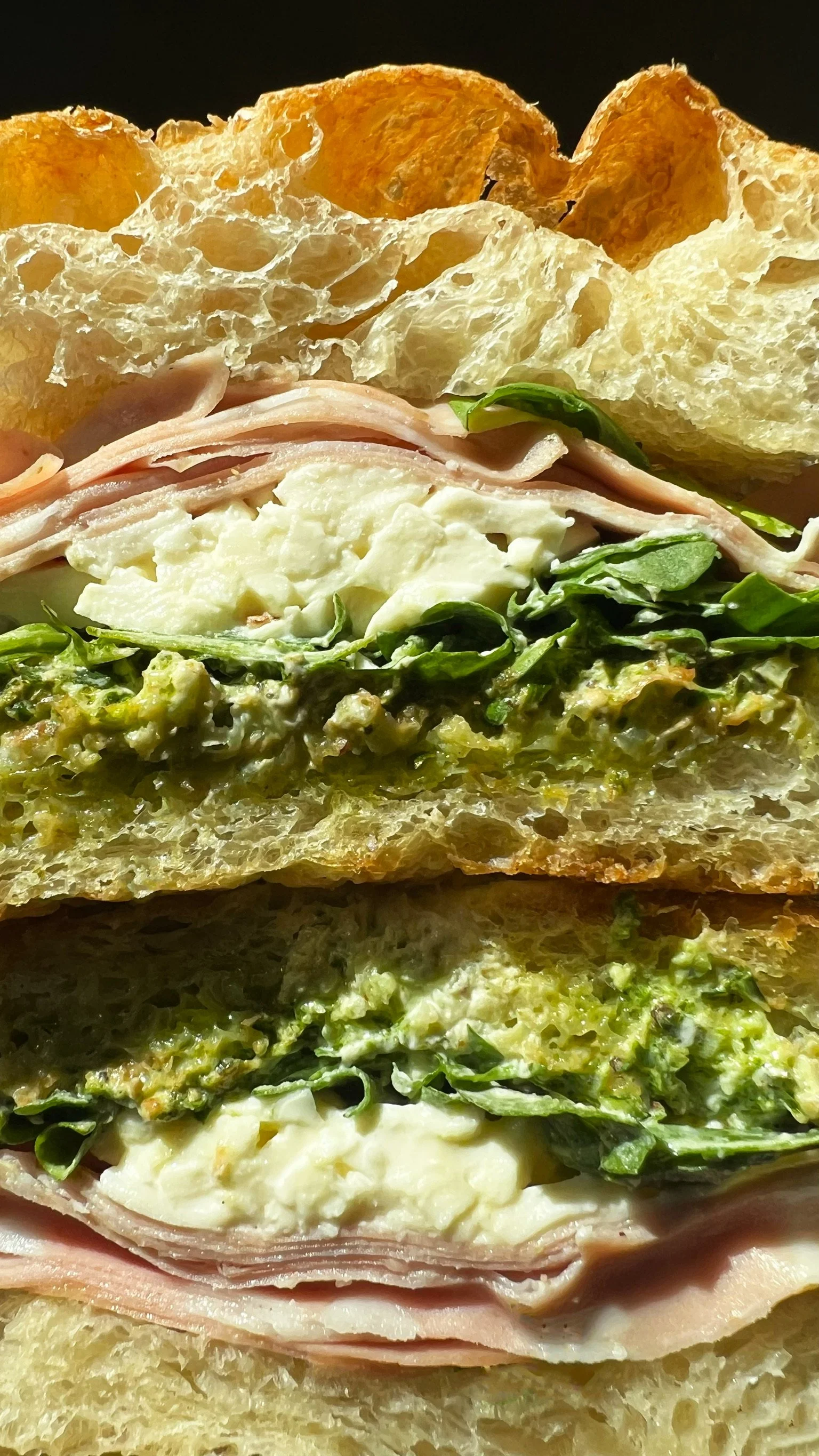 Close-up of a sandwich with bread, sliced turkey, scrambled eggs, spinach, avocado, cheese, and potato chips on top.
