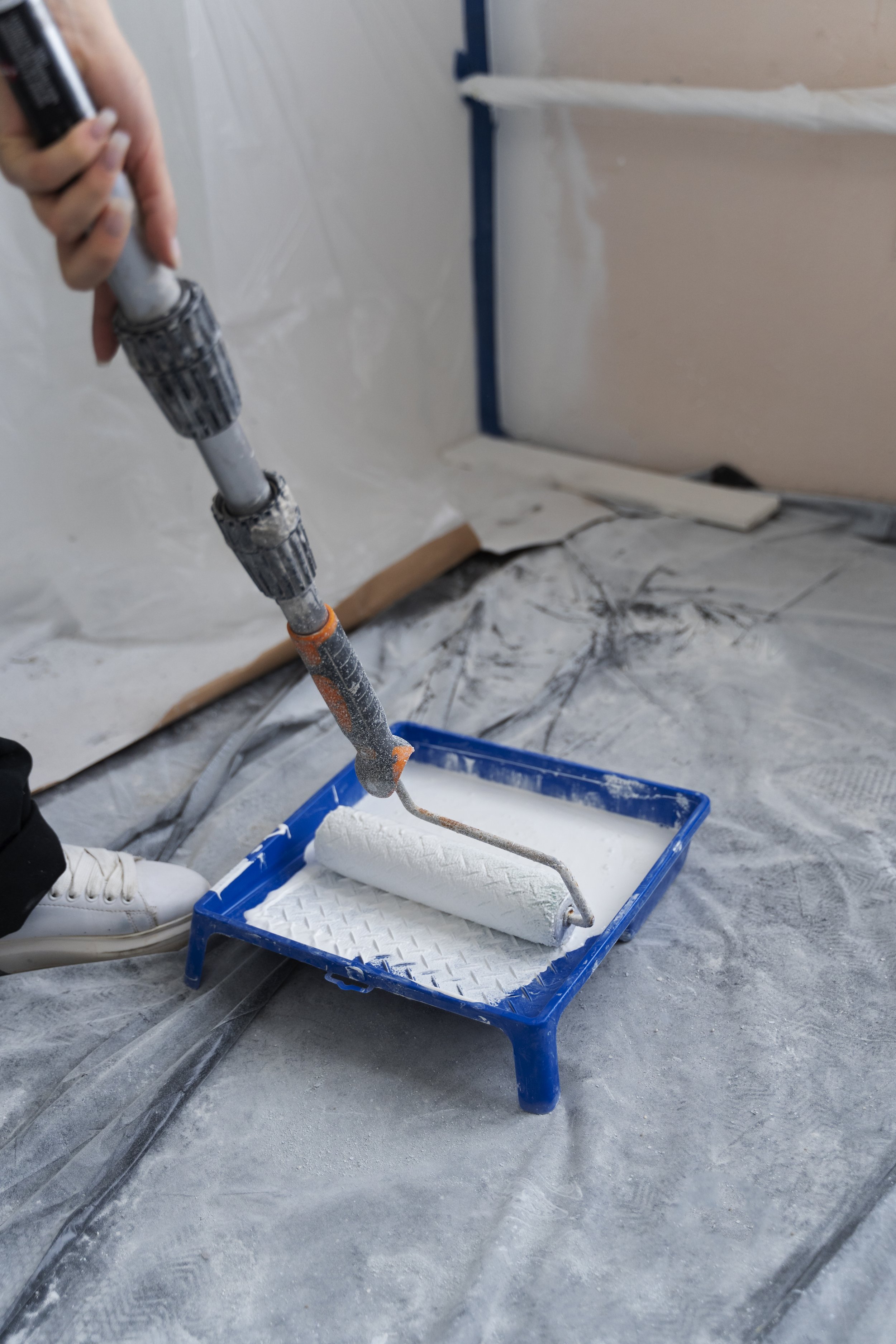 Person using a paint roller to apply white paint on a wall in a room under renovation.
