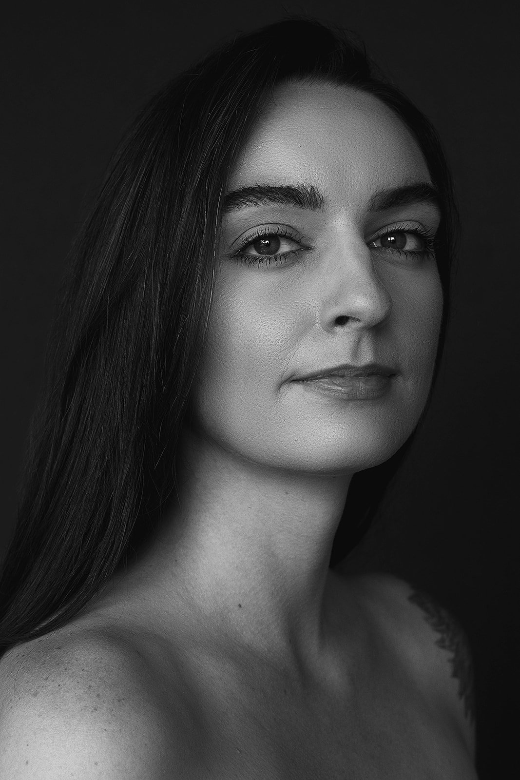 A black and white portrait of a woman with long dark hair, clear skin, and a calm expression, looking slightly to the side.
