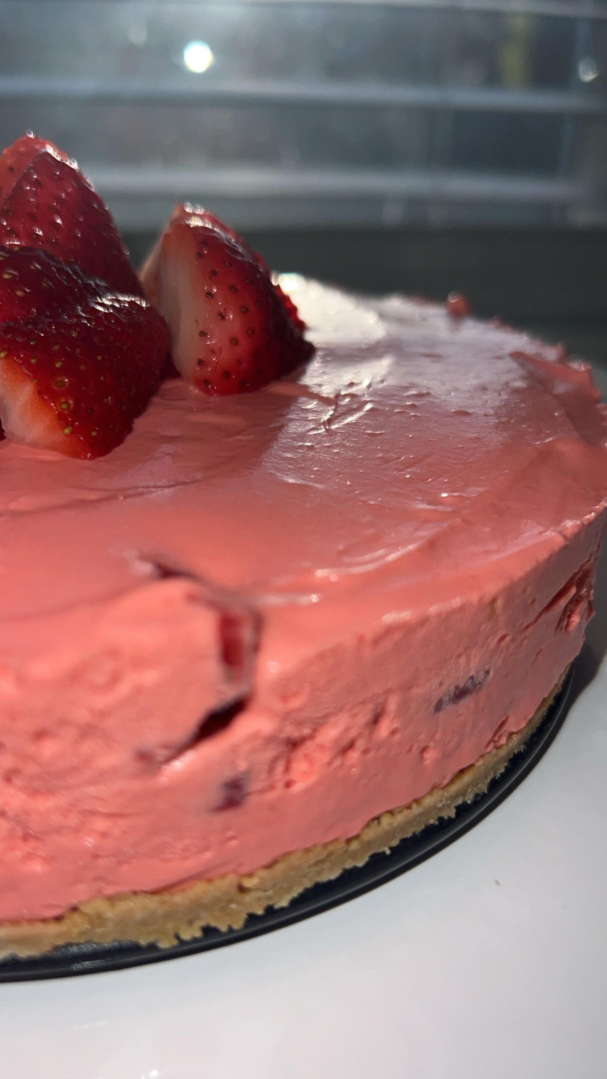Close-up of a creamy strawberry cheesecake with fresh strawberry slices on top, showing the pink filling and graham cracker crust.