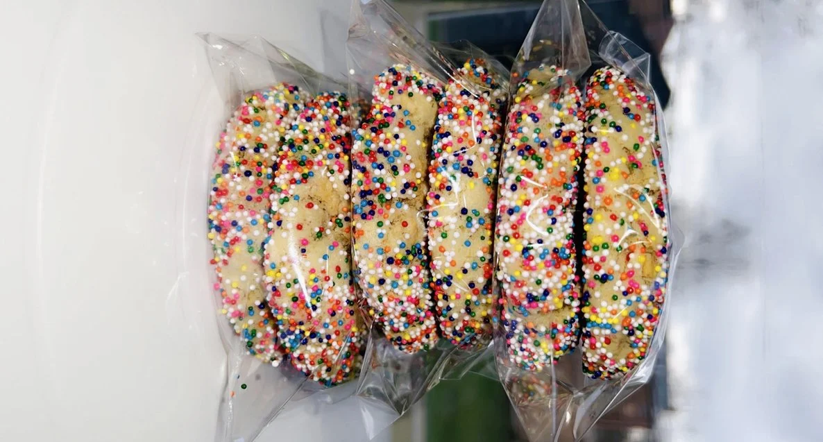 Six cookies covered in colorful sprinkles, wrapped in clear plastic.