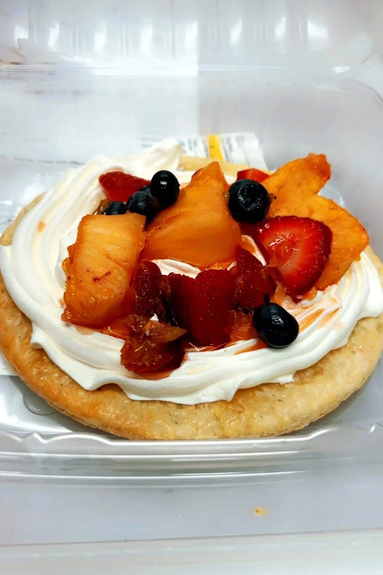Fried pie topped with whipped cream and mixed fresh fruit including strawberries, blueberries, pineapple, and peaches.