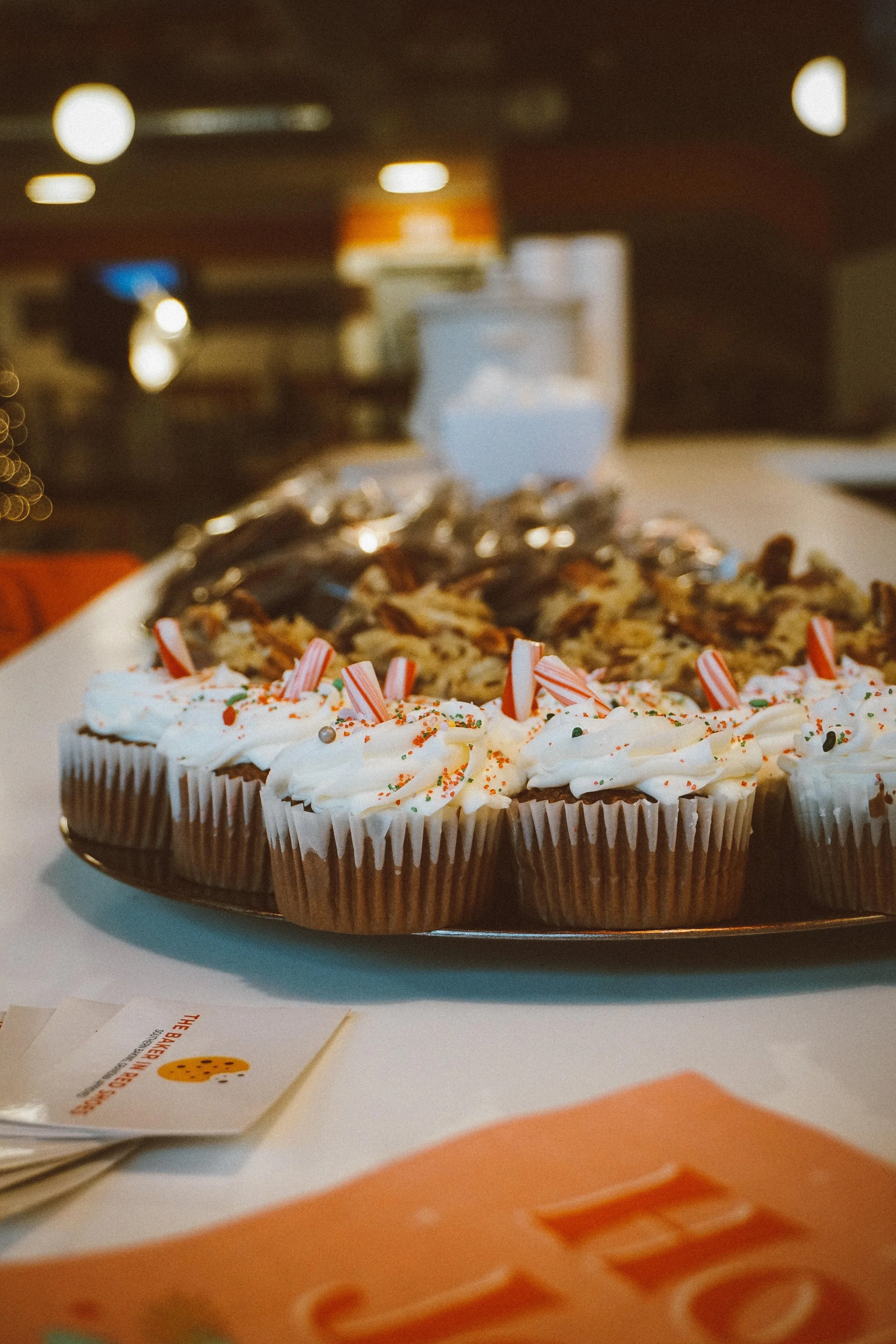 Cupcakes decorated with white frosting, colorful sprinkles, and candy canes on a tray.
