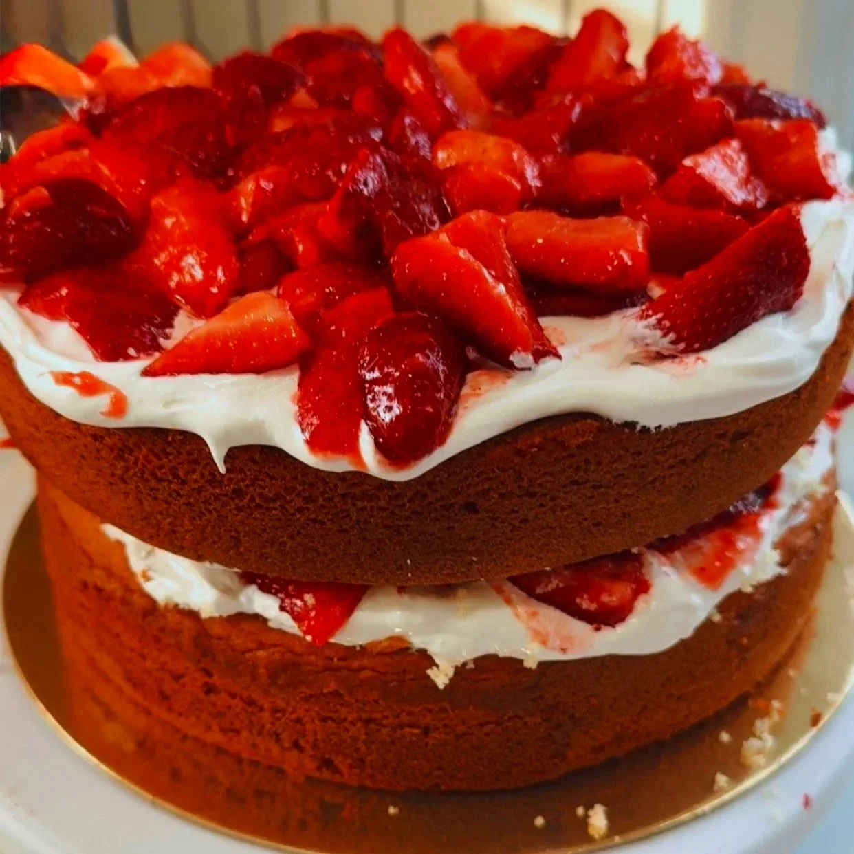 A close-up of a two-layer chocolate cake with white cream and sliced strawberries on top