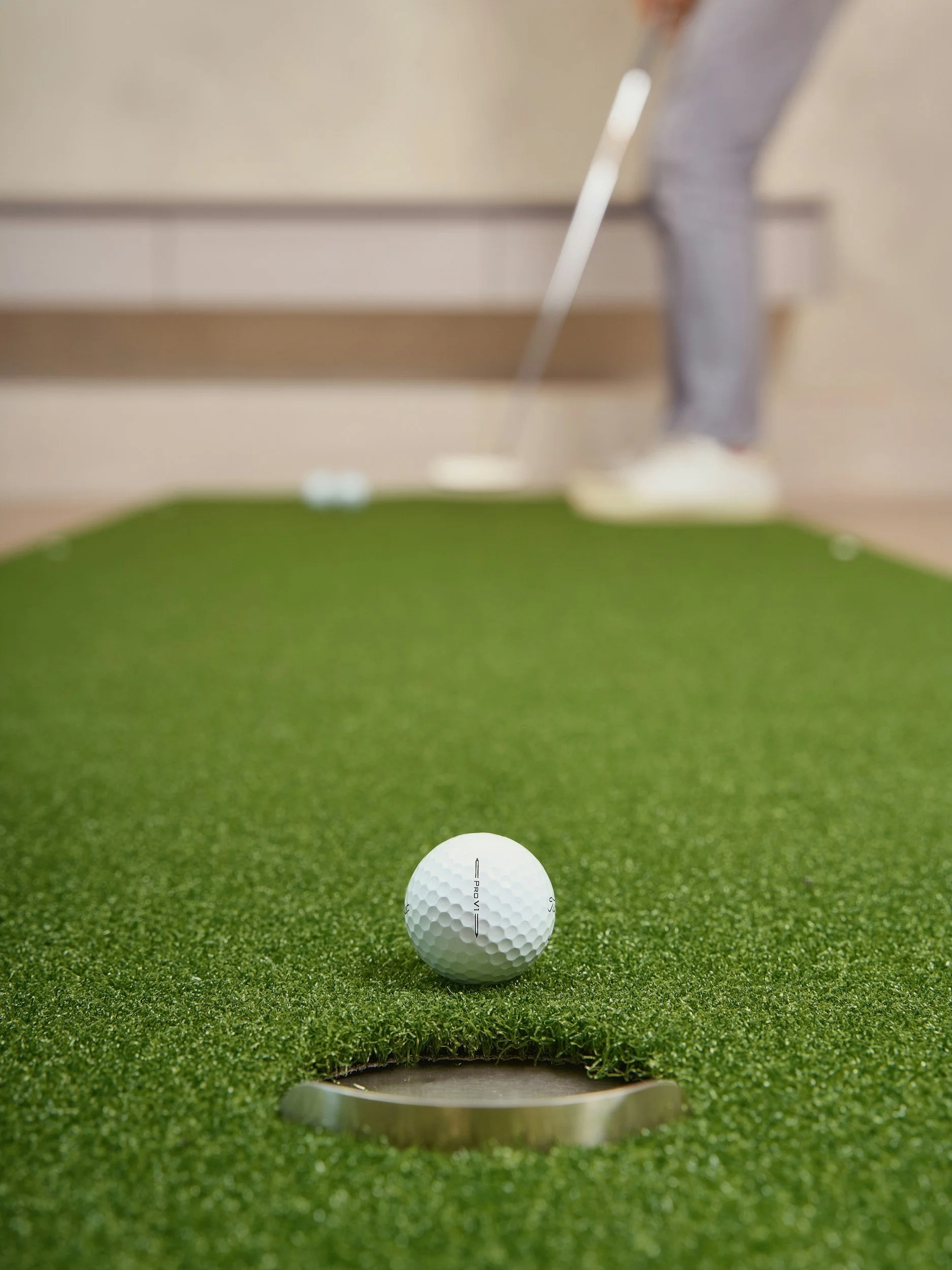 Golf ball placed on an artificial green near the hole, with a person in the background preparing to putt.
