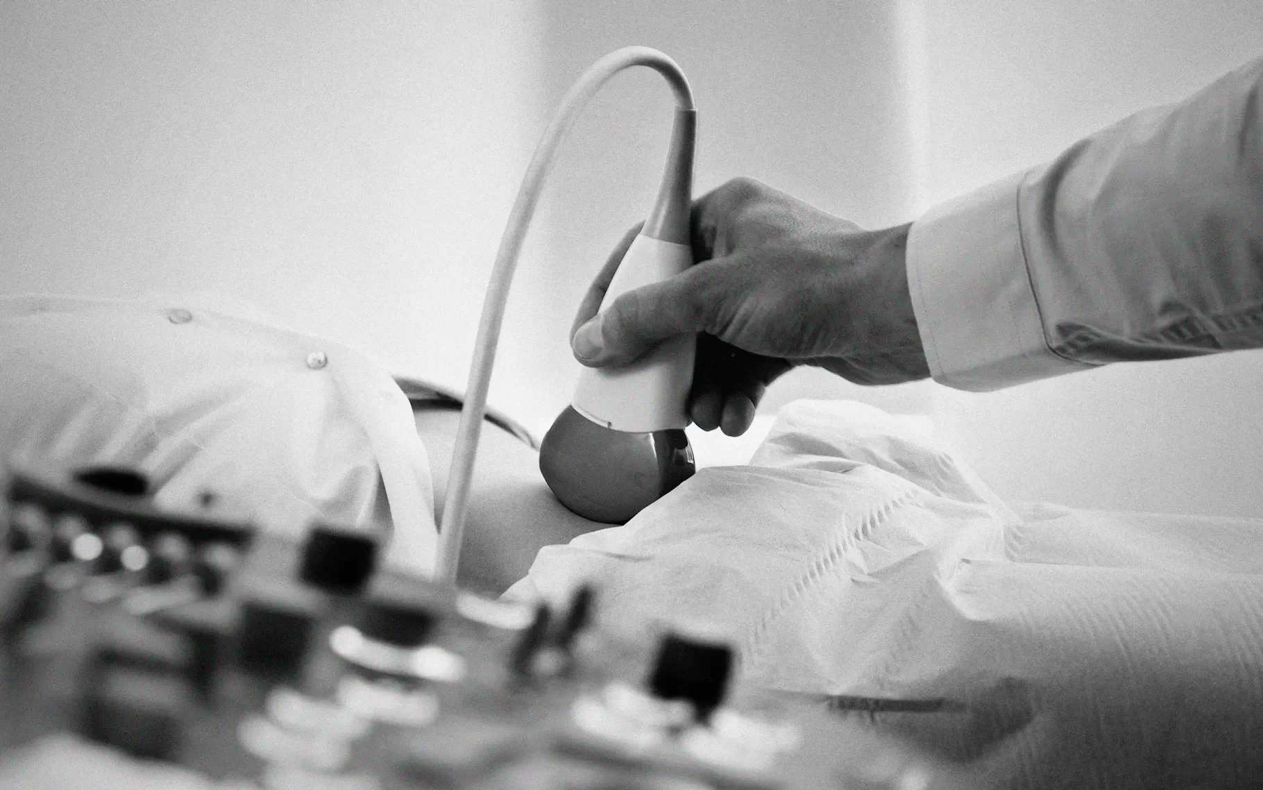A medical professional uses an ultrasound probe on a patient's abdomen, which is covered with a drape, during a medical examination.