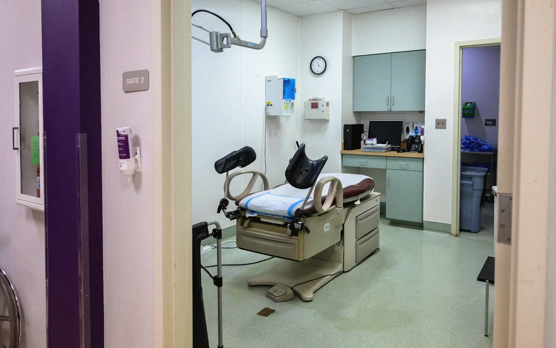 Hospital room with medical examination bed, computer, cabinets, and medical equipment.