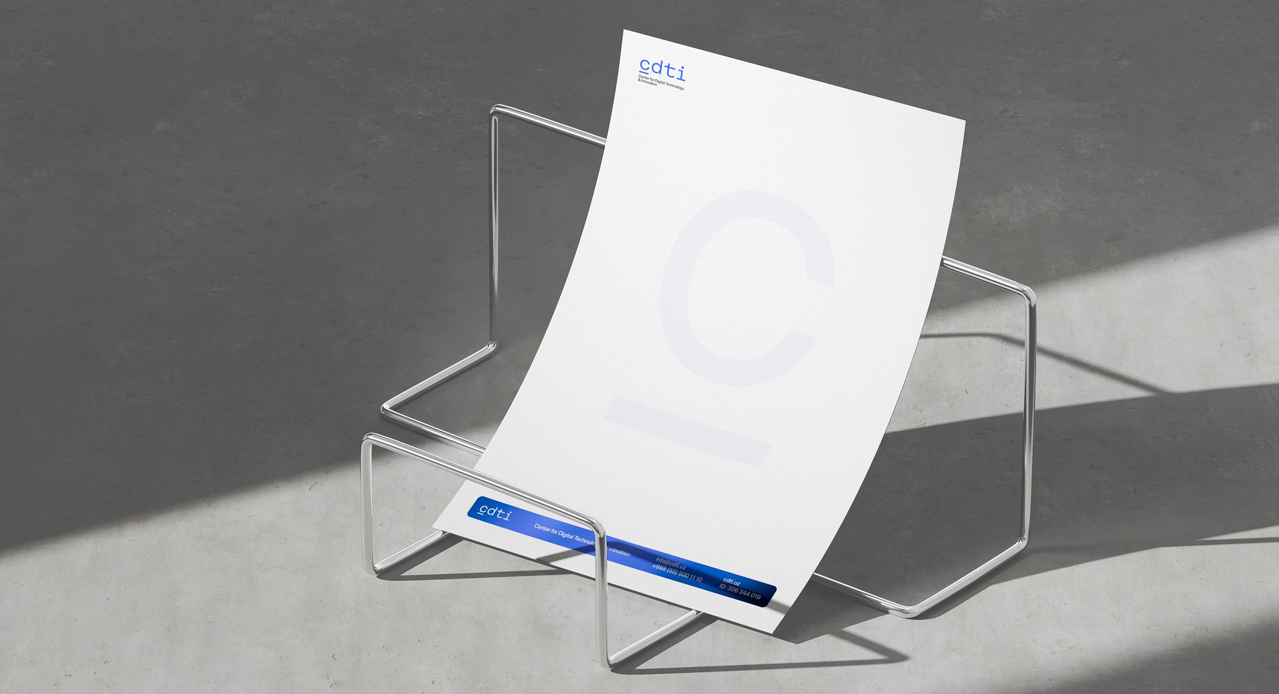 A minimalist metal magazine rack holding a large white sheet of paper with the words "Center for Digital Technology" and a large letter "C" visible on it, on a background with a shadow cast on a textured wall.