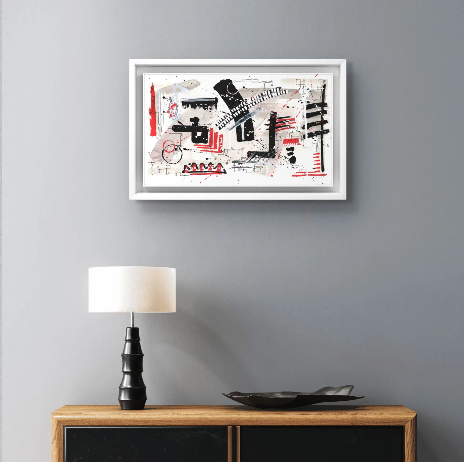 Tableau abstrait avec lignes noires, rouges et touches de beige dans un cadre blanc, accroché sur un mur gris.