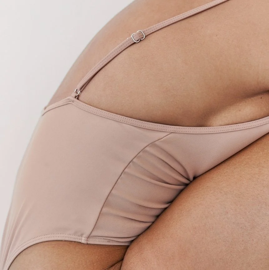 Close-up of a woman's torso wearing beige lingerie, showing part of her side and stomach.