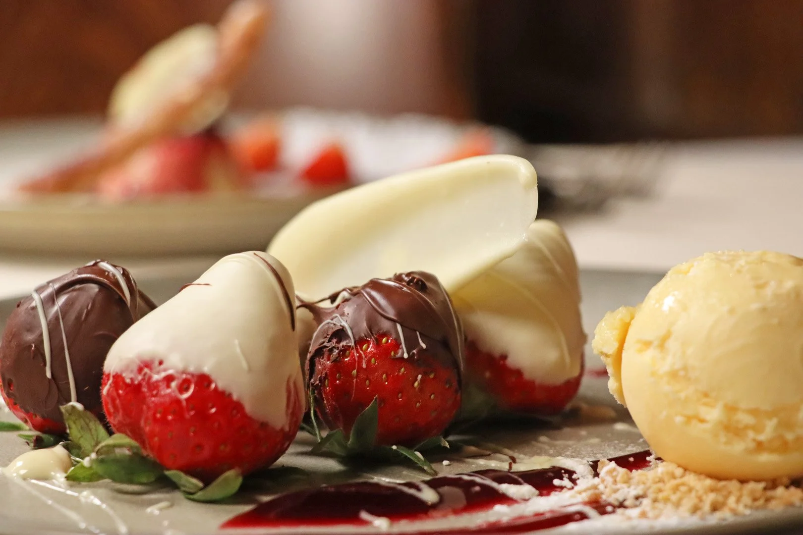 Close-up of strawberries dipped in white and milk chocolate, with a scoop of vanilla ice cream on the side.