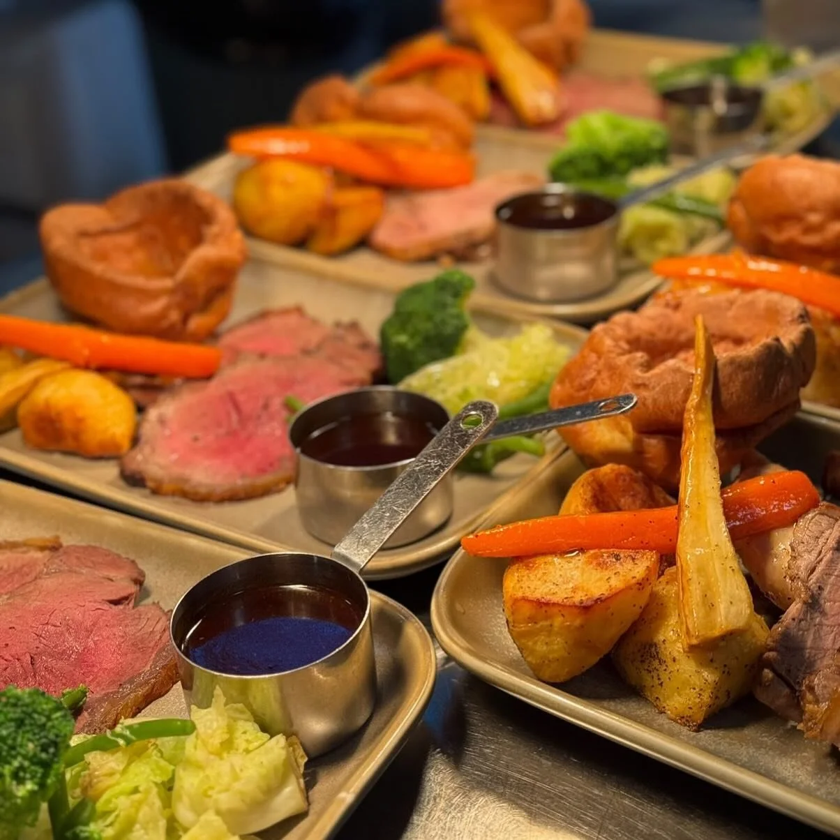 Plates of roasted meats, vegetables, and dipping sauces, including carrots, broccoli, roasted potatoes, and various cuts of beef or lamb.