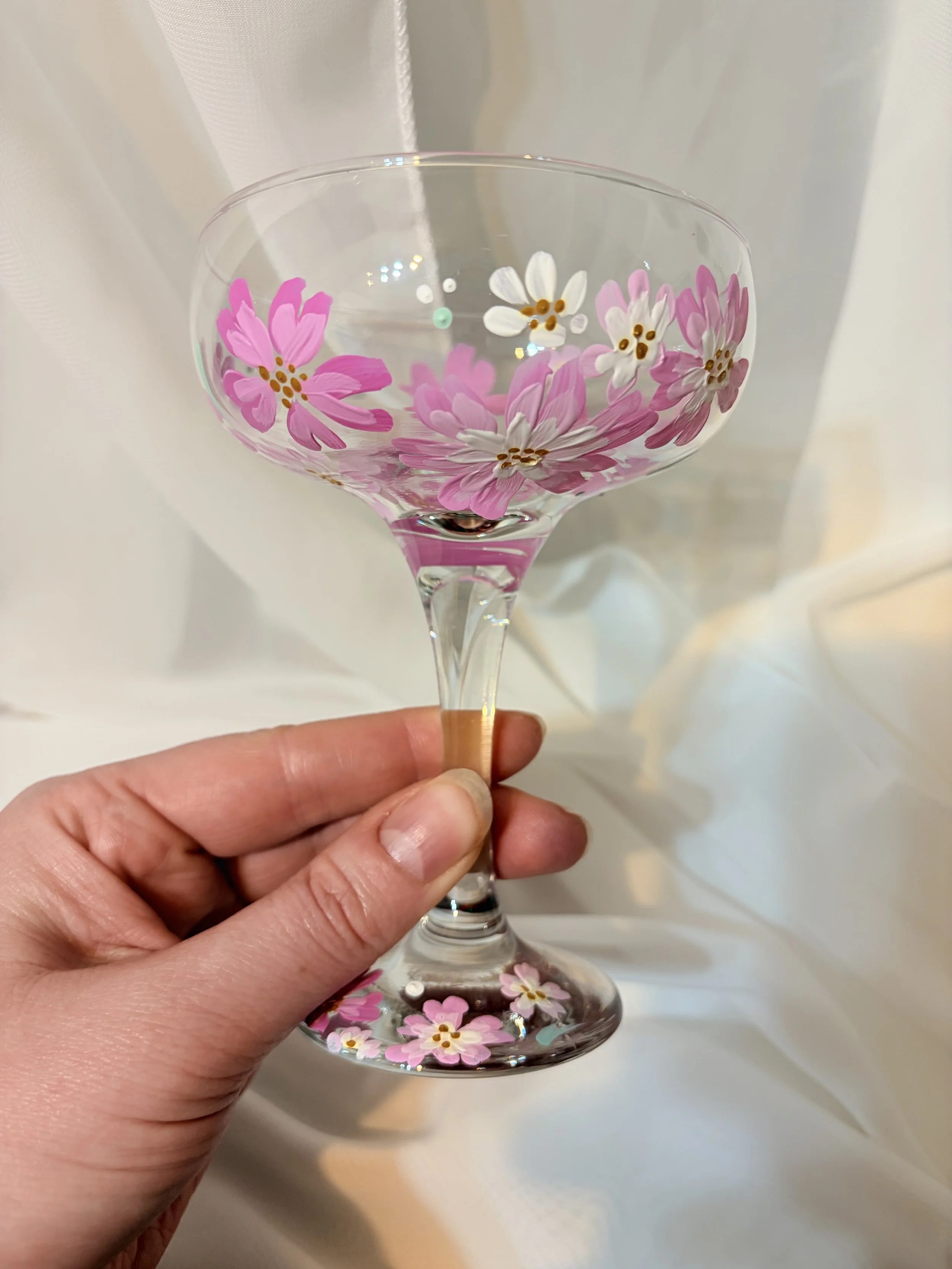 Hand holding a glass with pink and white floral designs, against a white background.
