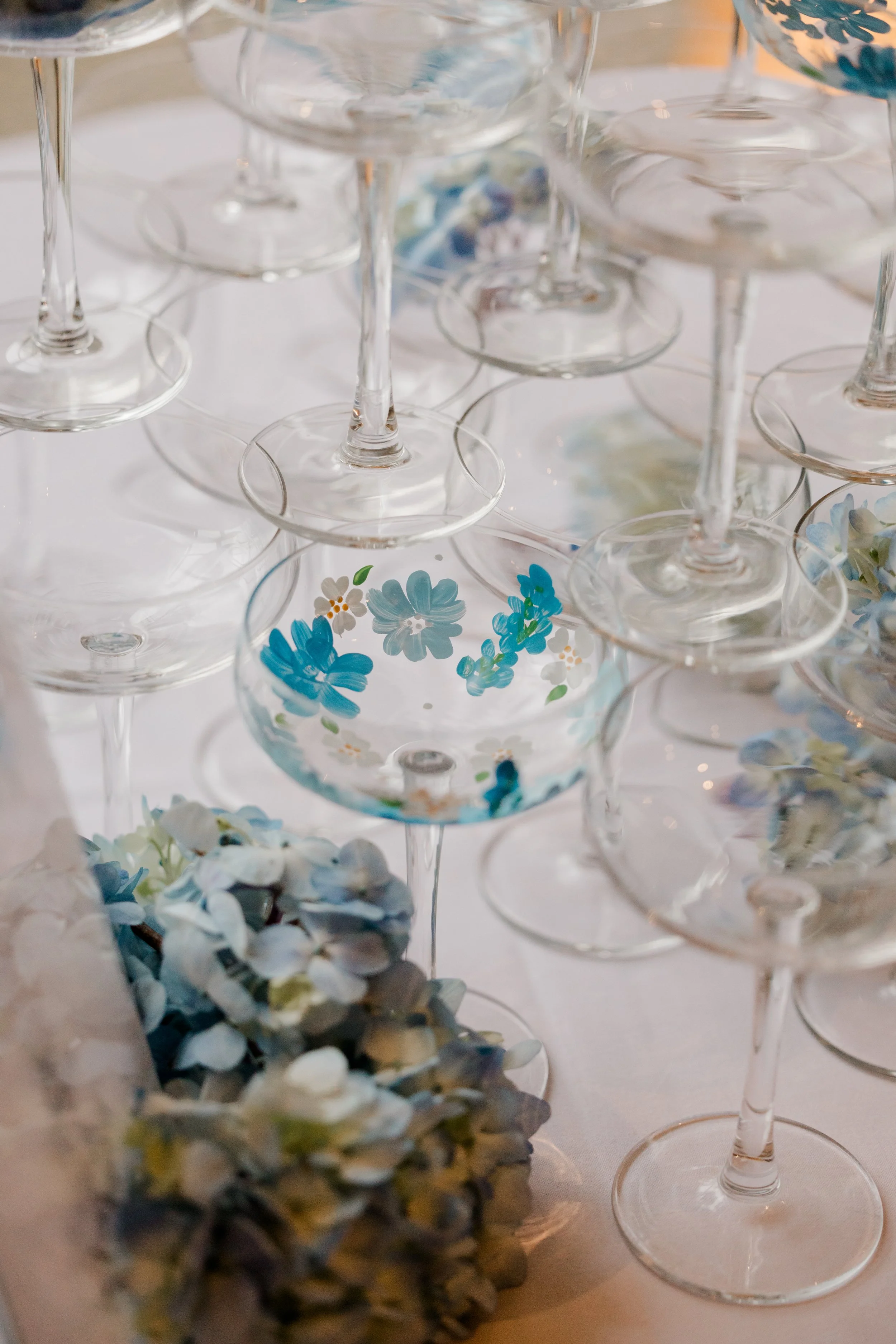 Multiple empty and decorated wine glasses arranged on a table with a cluster of blue and white flowers.