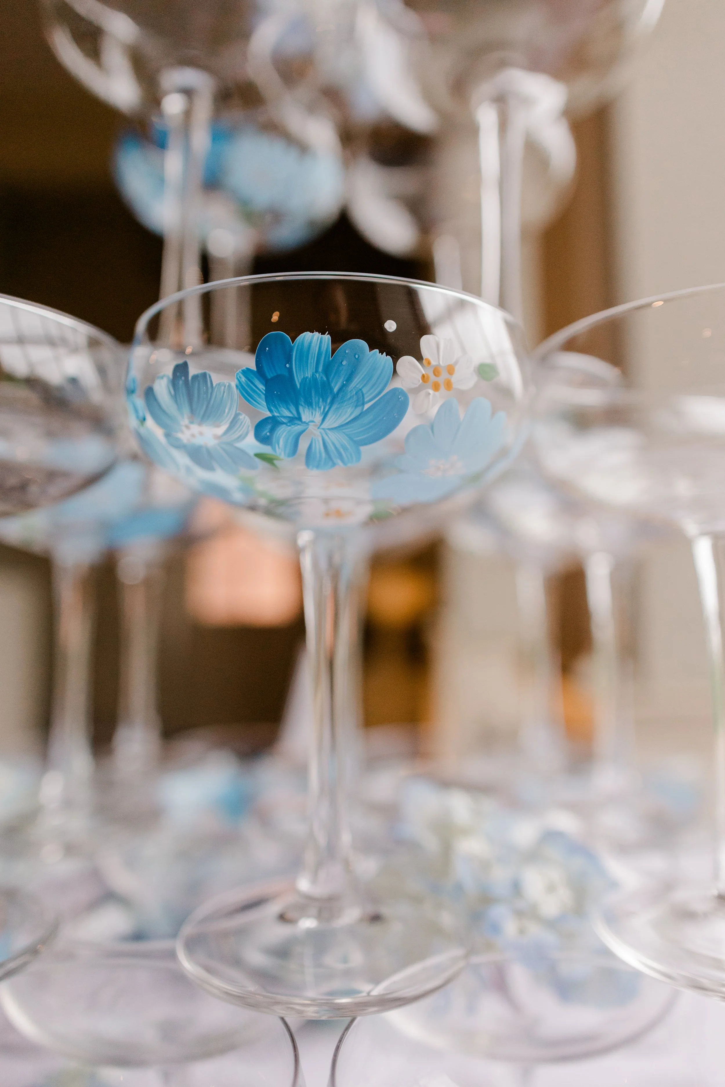 A collection of empty cocktail glasses with blue floral designs painted on the rims, arranged on a surface.
