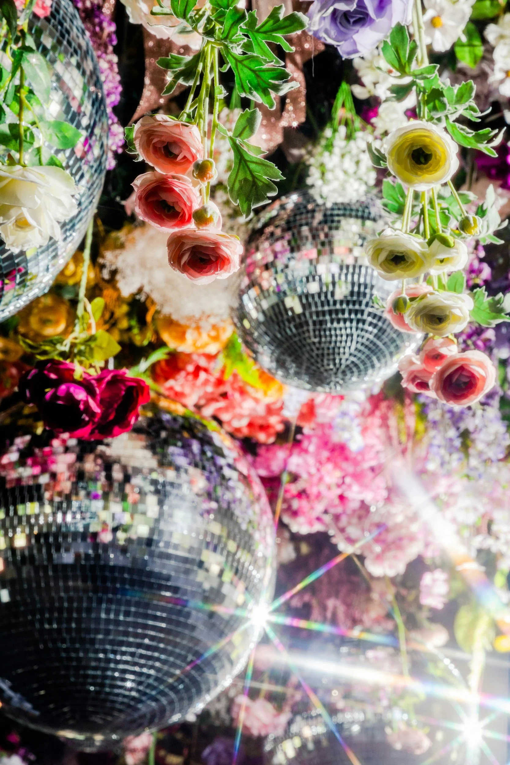 Colorful flowers and disco balls hanging overhead with reflections.